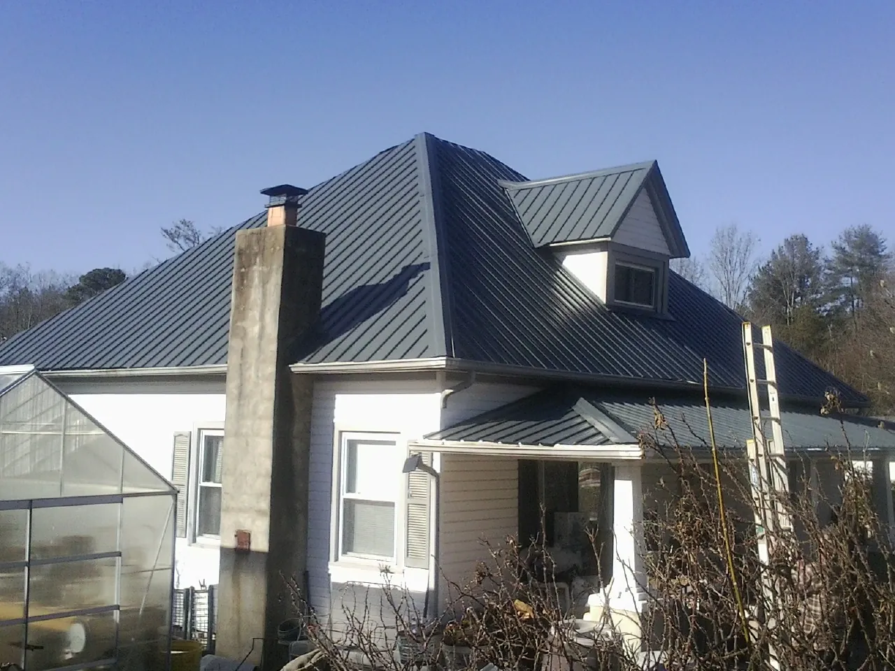 Dark blue standing seam metal roof on a white farmhouse with dormer — Slate & Tile Roof Repair by Roofing Brothers in Sneads Ferry