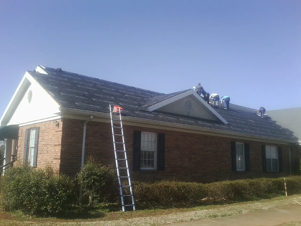 Crew tearing shingles off a brick ranch roof with a ladder set — Emergency Roof Repair work by our crew in Sneads Ferry