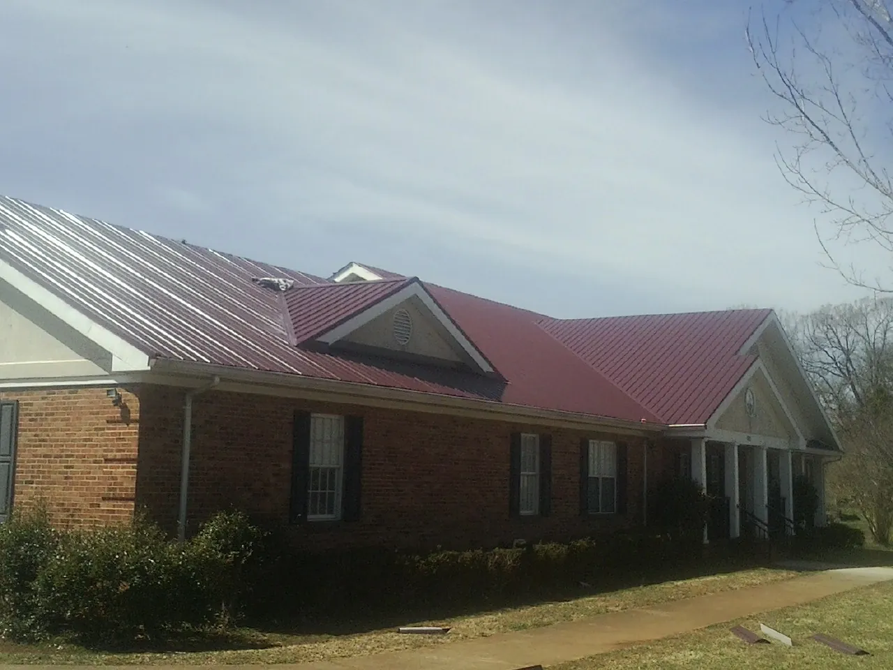 Red metal roof with gabled entries on a long brick building, from a Hail Damage Roof Repair job in Sneads Ferry