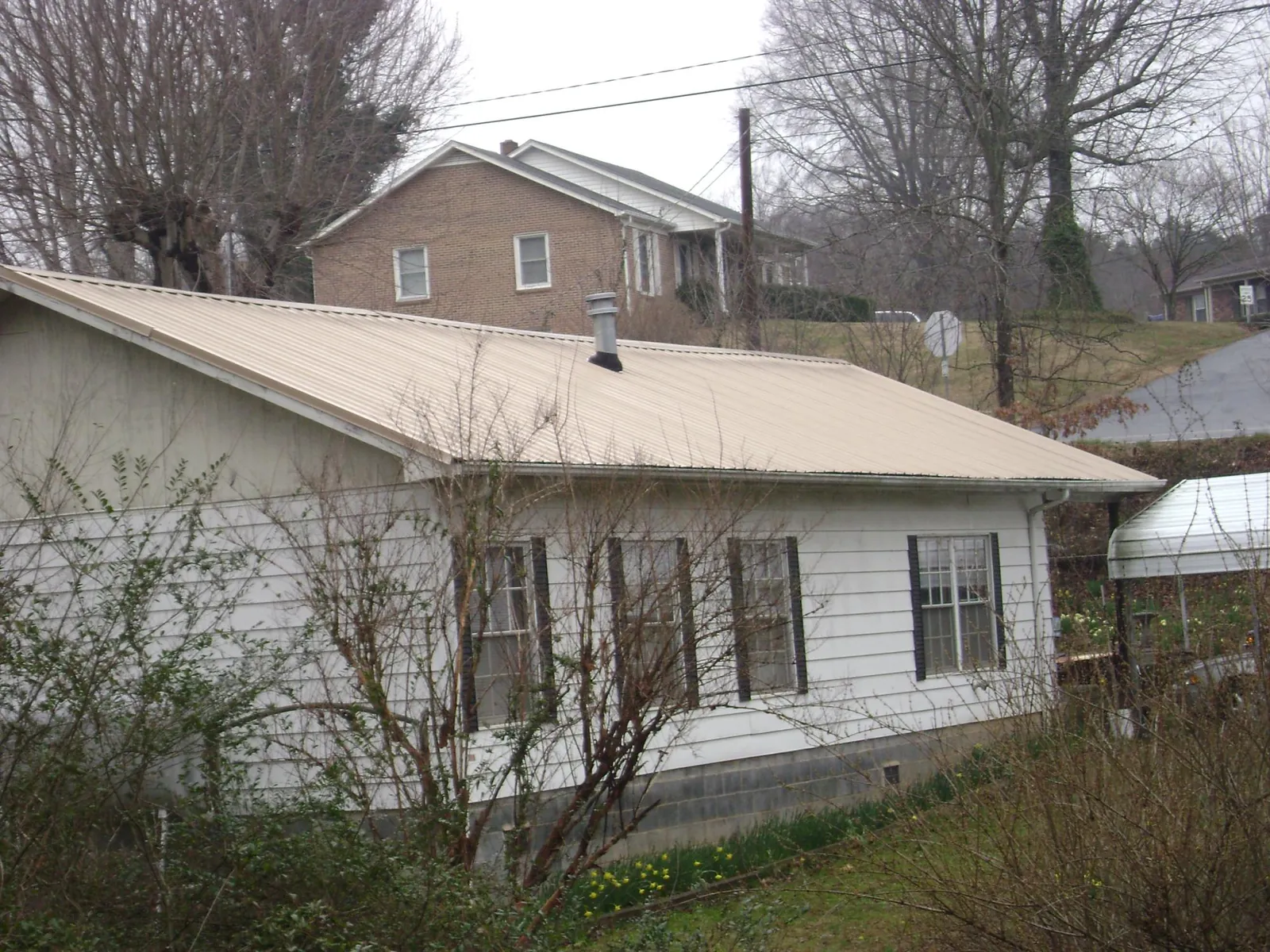 Tan metal roof on a white sided house set into a hillside — Commercial Roofing by Roofing Brothers in Sneads Ferry